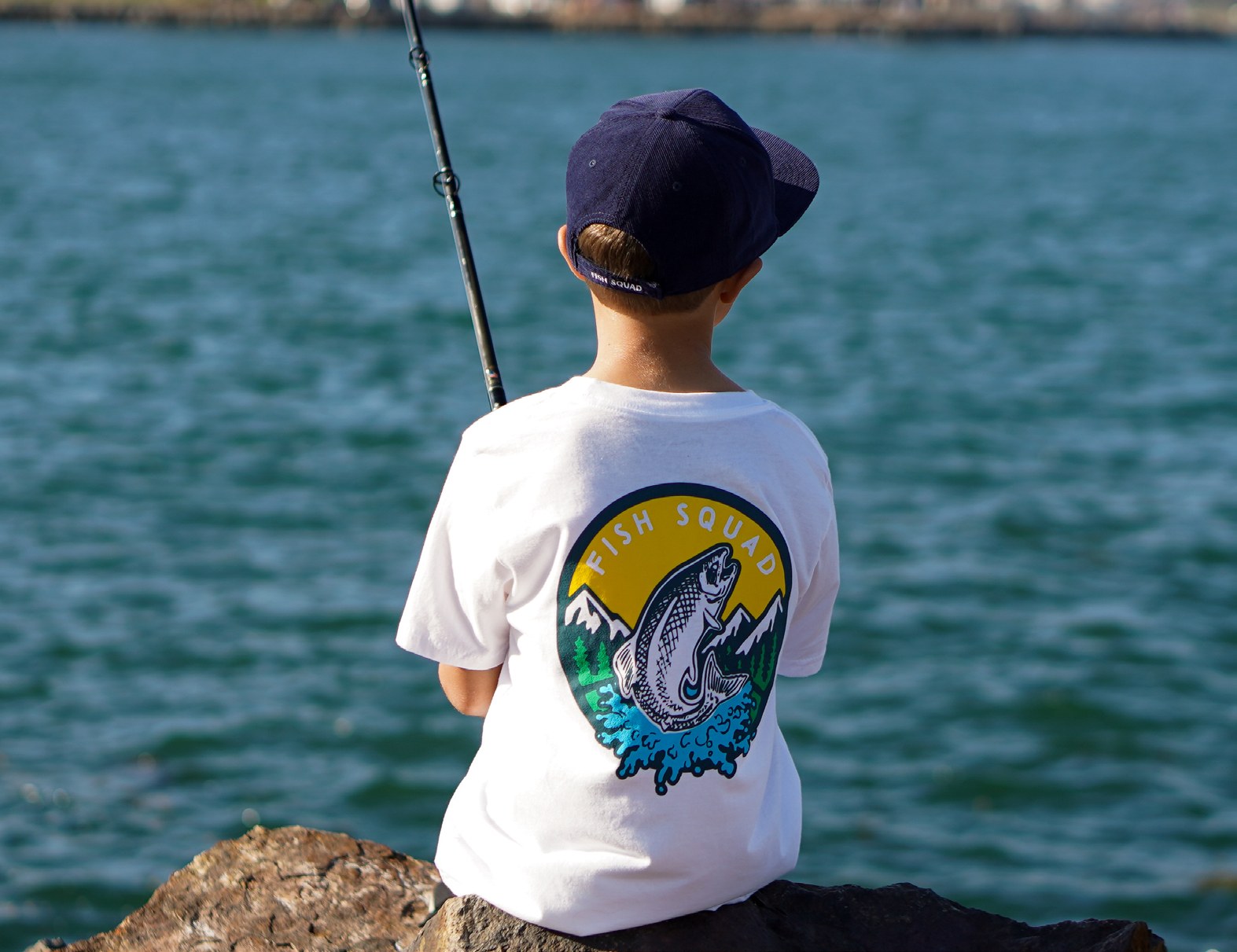 Young angler in a Fish Squad shirt fishing beside the water